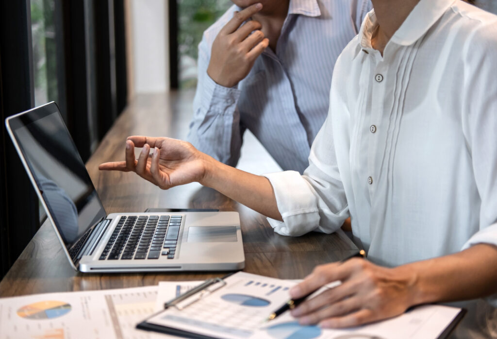 Two colleagues discuss data at a laptop in a bright office setting.