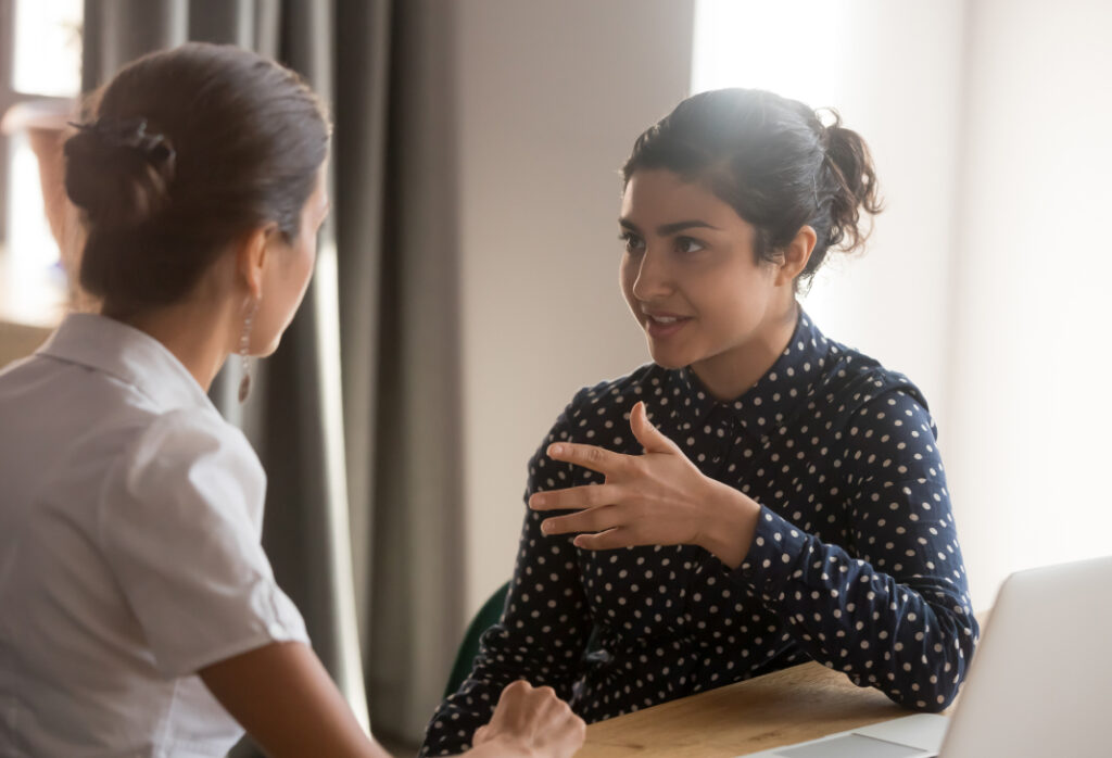 Two women engaged in a focused discussion at a workplace setting.