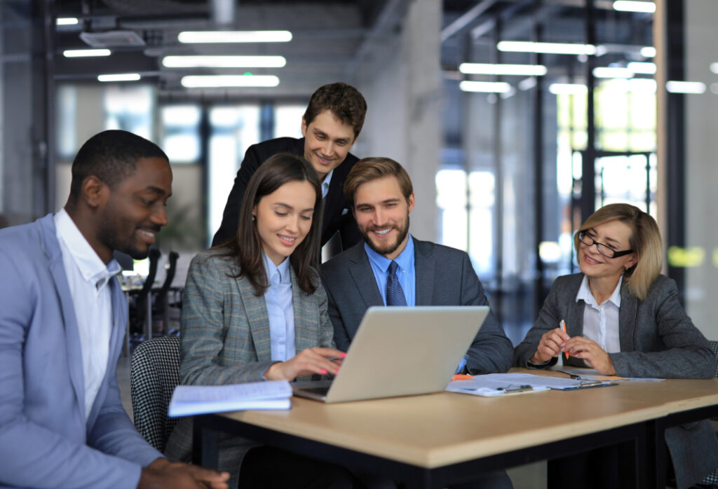 Team collaborating around a laptop in a modern office environment.