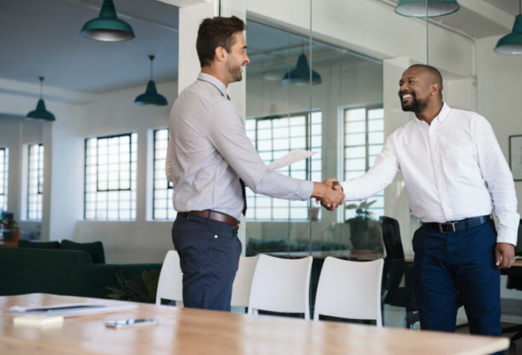 Two colleagues greet each other with a handshake in a modern office setting.