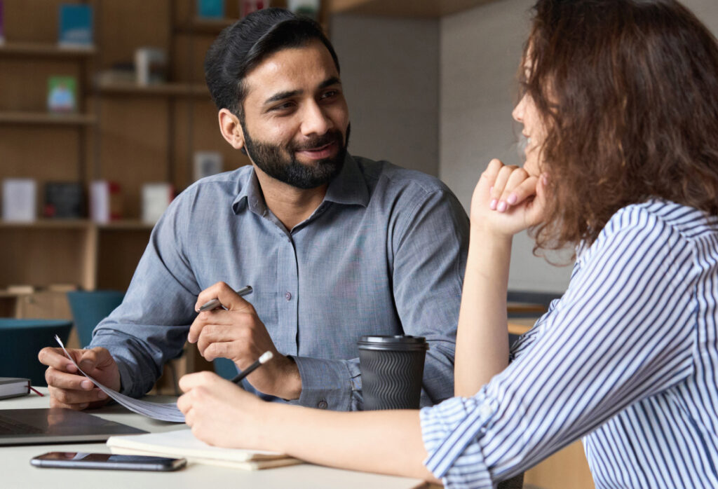 A man and woman discussing work over coffee in a modern office setting.