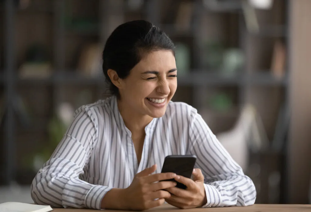 Smiling woman enjoying helpful interaction on smartphone at work desk.