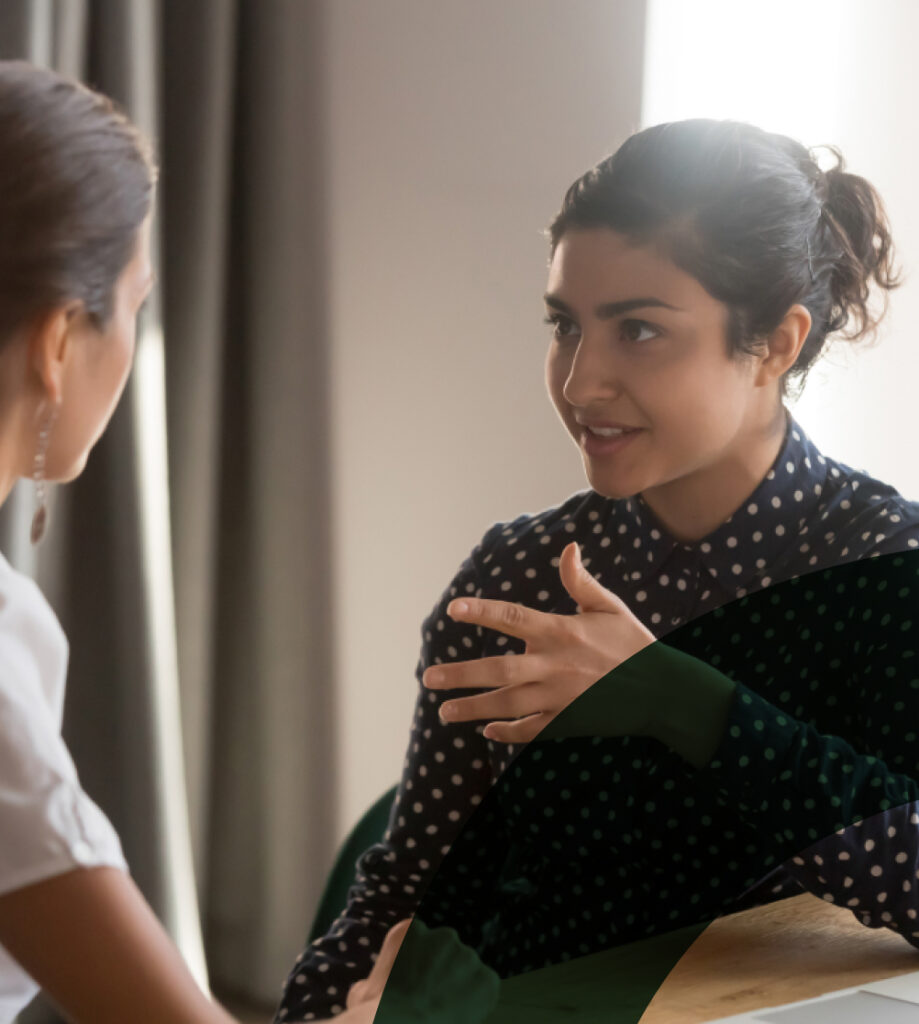 A woman in a polka dot shirt is talking to another person indoors.