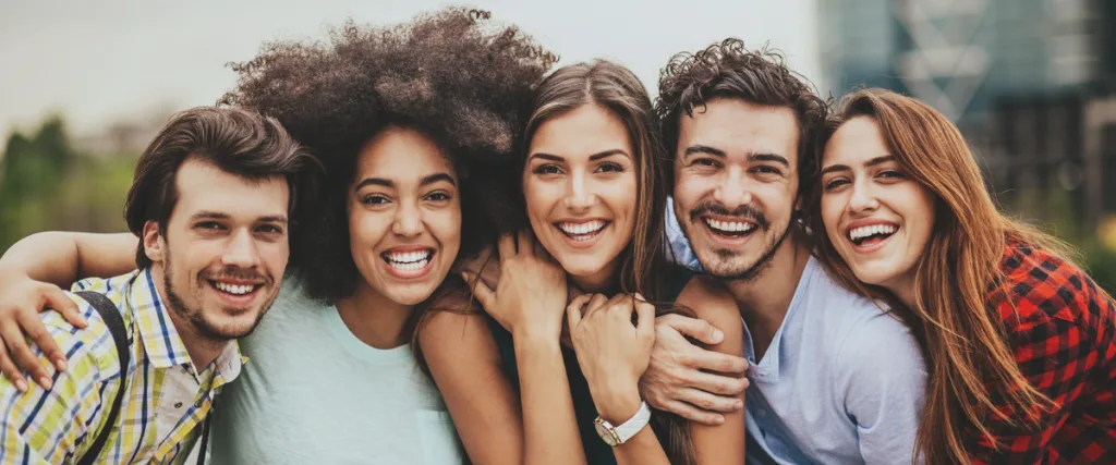 A diverse group of five smiling people standing closely outdoors.