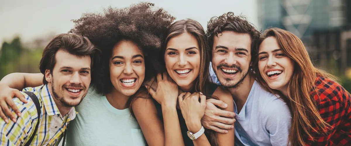 A diverse group of five smiling people standing closely outdoors.