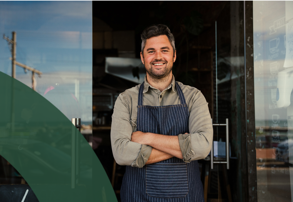 Smiling employee in apron stands confidently at a storefront entrance.