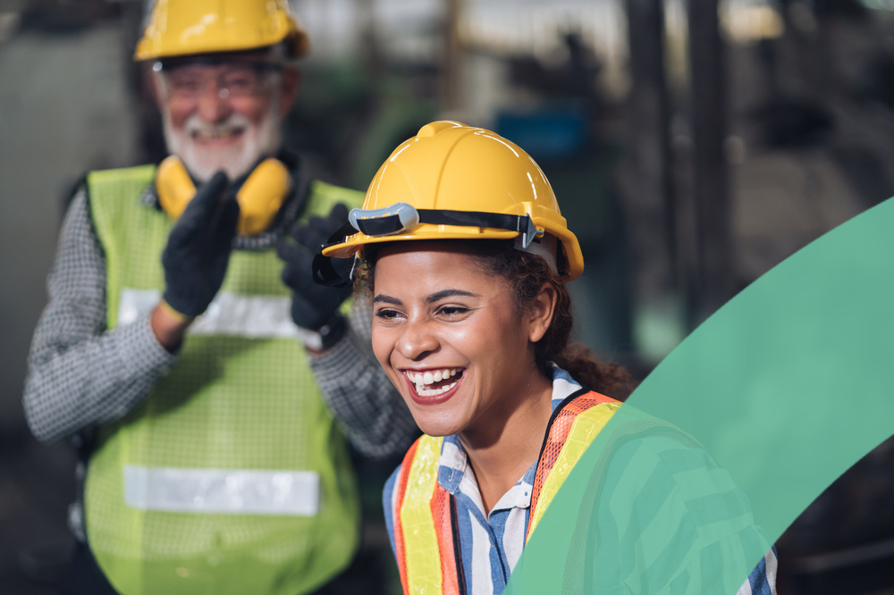 Two workers in safety gear smiling and engaging in an industrial setting.