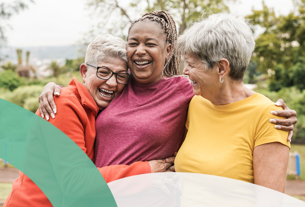 Three women happily embrace outdoors, showcasing supportive friendship.