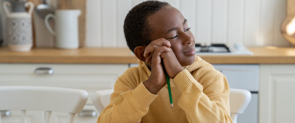 Child in a cozy sweater looks thoughtfully while holding a pencil.