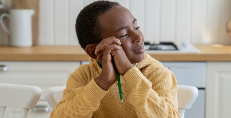 Child in a cozy sweater looks thoughtfully while holding a pencil.