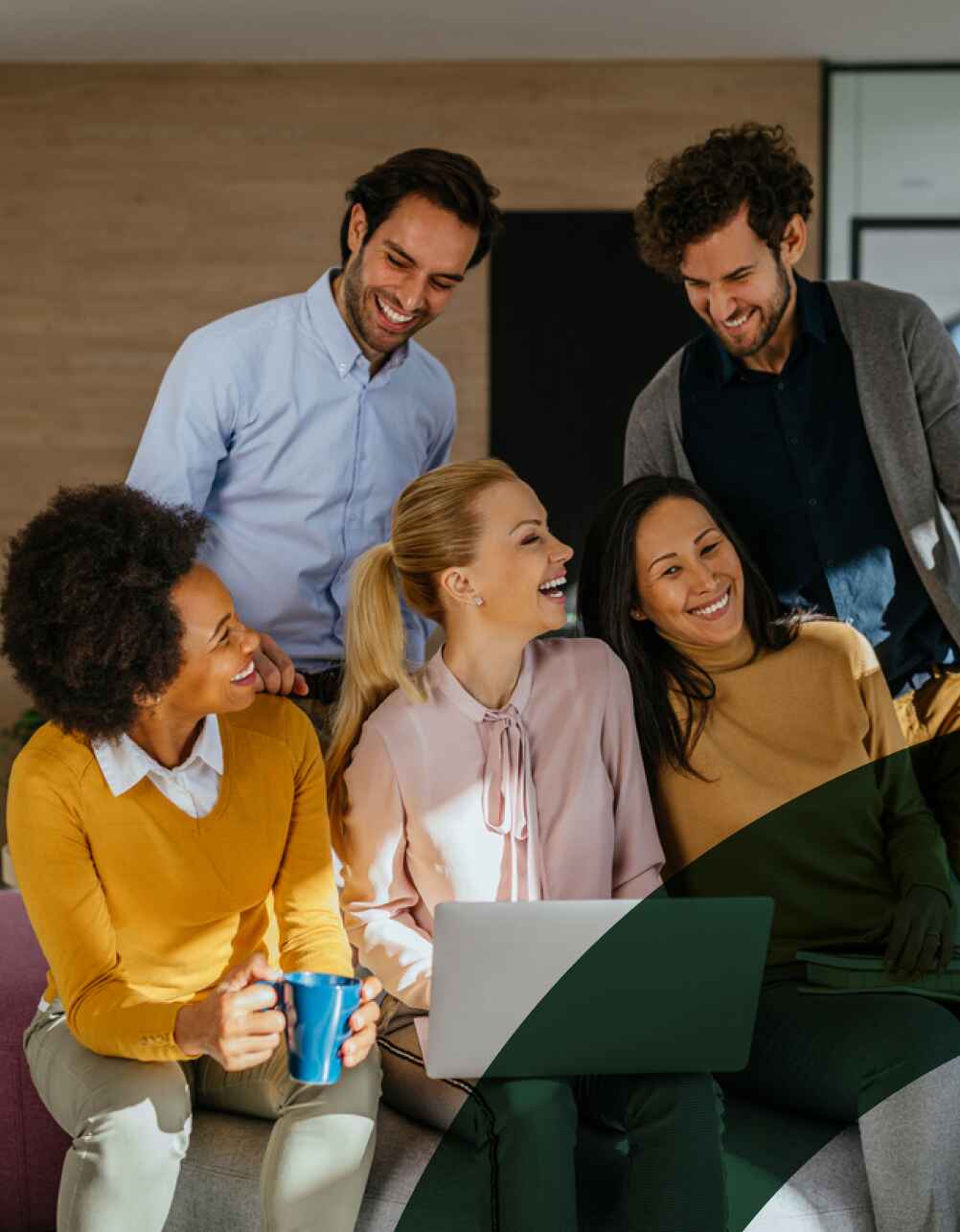 A group of diverse colleagues laughing together on a comfortable grey couch.